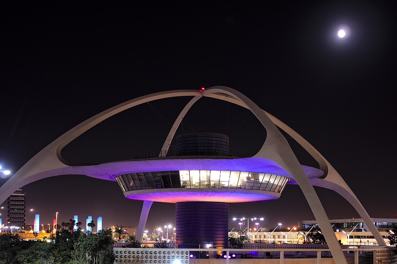 A concrete building shaped like a saucer held up on four crossed white legs, moon in the sky above it.