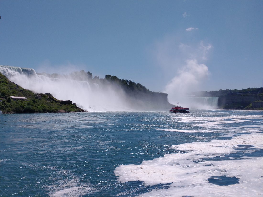 A red tour boat approaches the mist of Niagara Falls, with both cascades visible