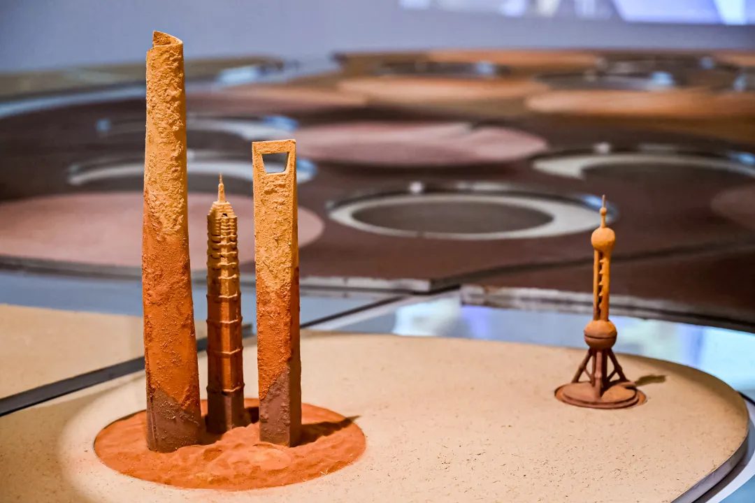 Shanghai skyline rendered in rammed earth — the Jin Mao Tower, Shanghai World Financial Center, and Oriental Pearl Tower as miniature soil sculptures