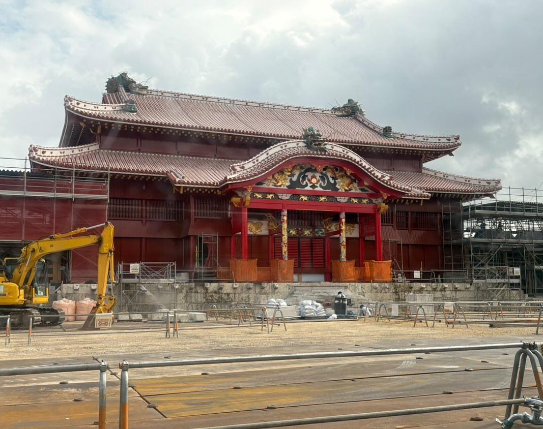 首里城正殿、再建工事中。赤瓦の屋根と朱の柱、足場と重機、手前に鉄板敷きの工事ヤード。2025年12月23日 / Shuri Castle Seiden under reconstruction with scaffolding and site plating in the foreground, 23 December 2025.
