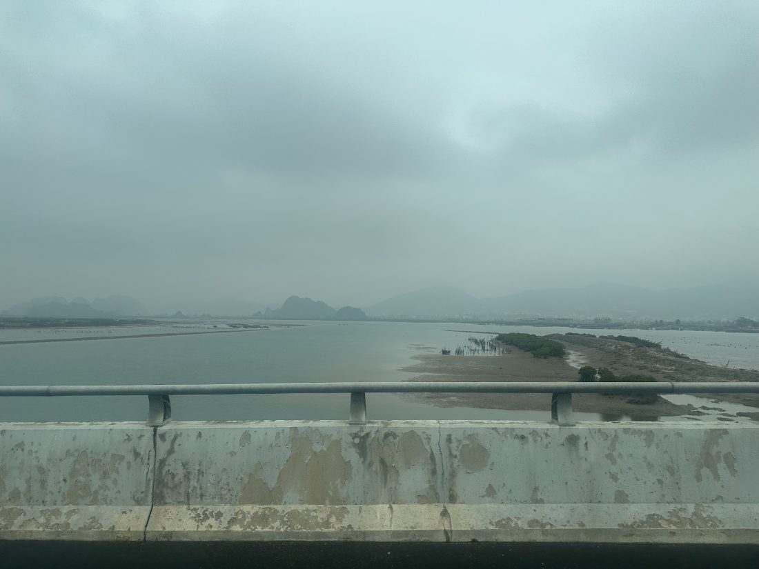 Bridge guardrail over silted estuary with limestone karst in distance