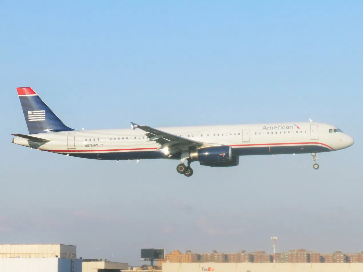 American Airlines Airbus A321 still wearing the US Airways tail livery, landing gear down against a clear sky.