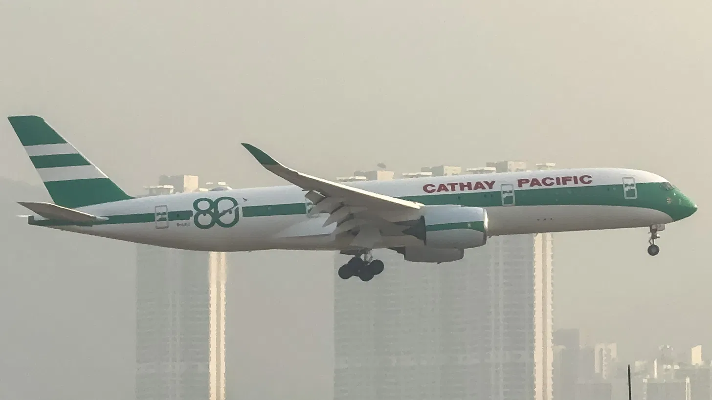 Cathay Pacific Airbus A350 in the 80th anniversary livery, green and white 1960s-style stripes, an '80' on the forward fuselage, landing near Hong Kong towers in haze.