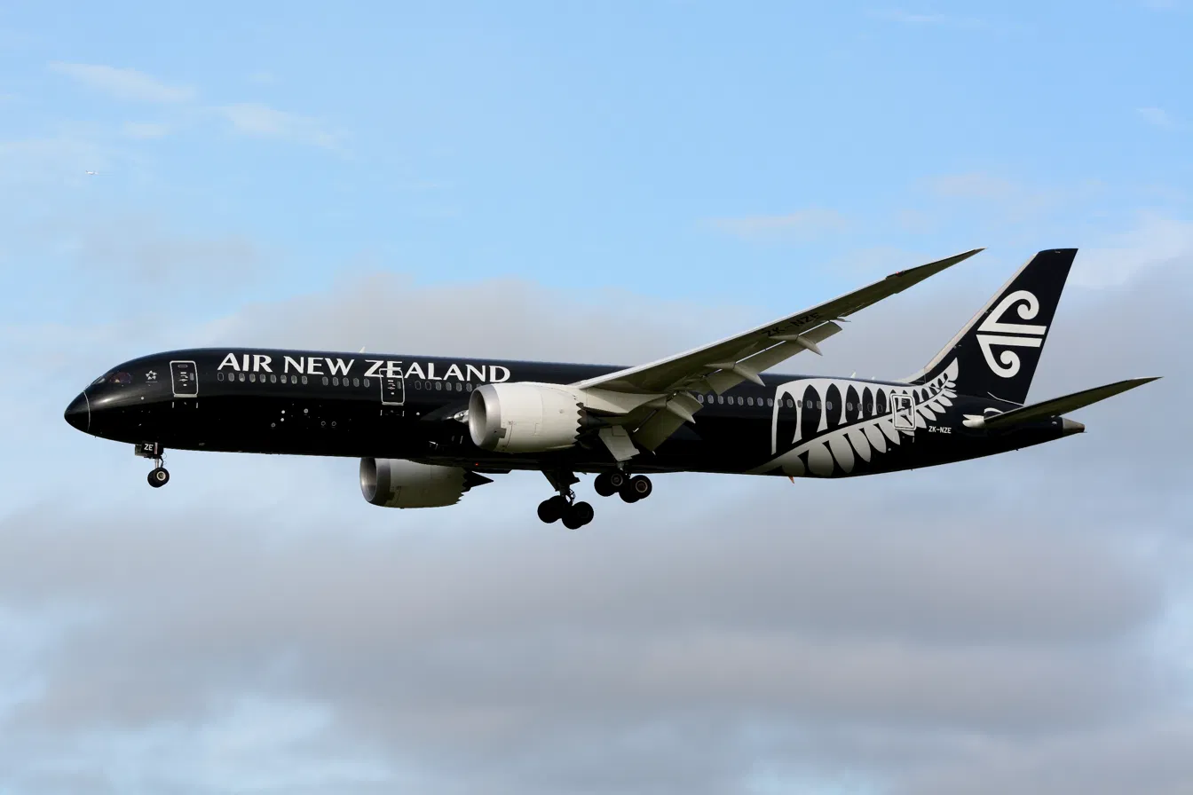 Air New Zealand Boeing 787-9 in all-black livery with a silver fern on the tail, landing gear down against a cloudy sky.