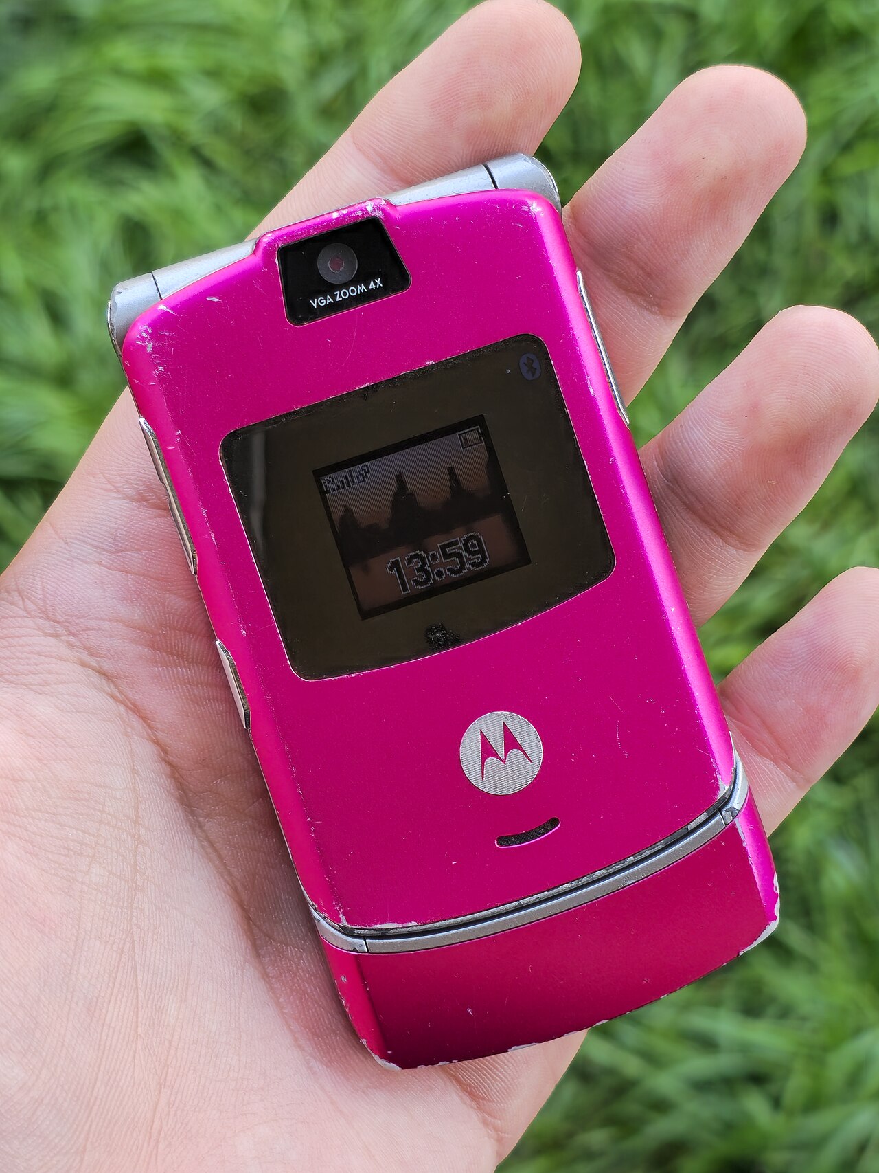 Slim pink Motorola RAZR flip phone, closed, photographed against white in an open hand