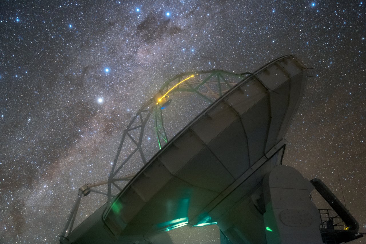 Photograph of the southern Milky Way at night: bright star clouds crossed by dark dust lanes, above a telescope dome.