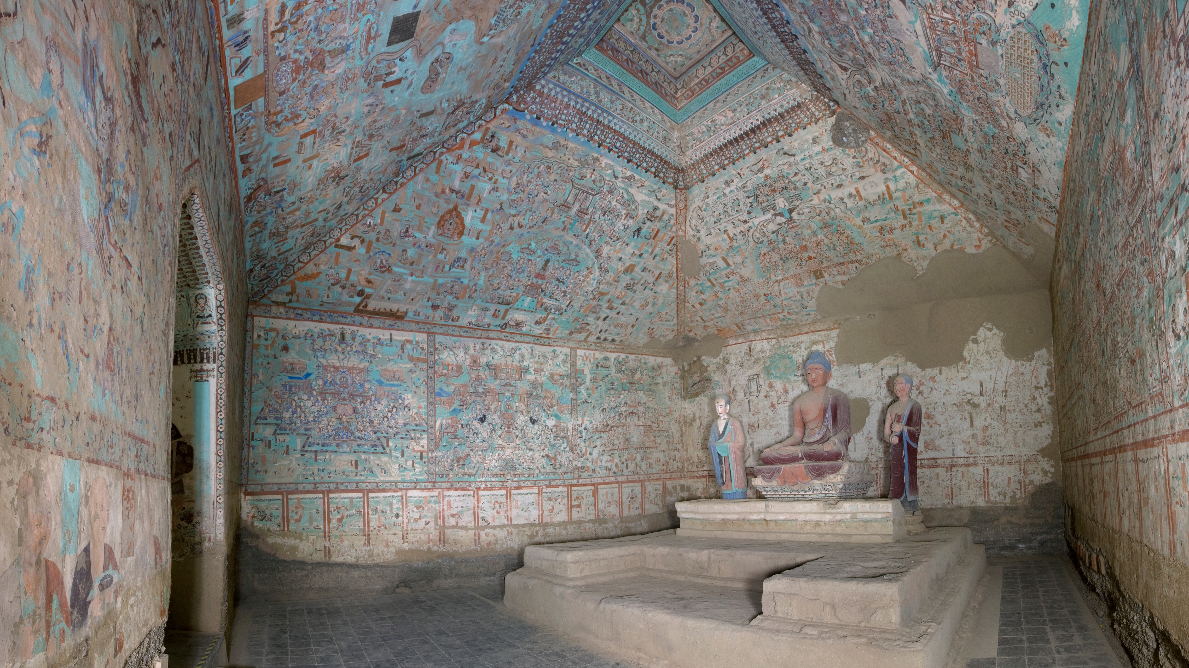 Cave 85 main chamber after conservation: painted ceiling and walls in blue-green pigments, with a seated Buddha and two attendant figures on the altar platform.