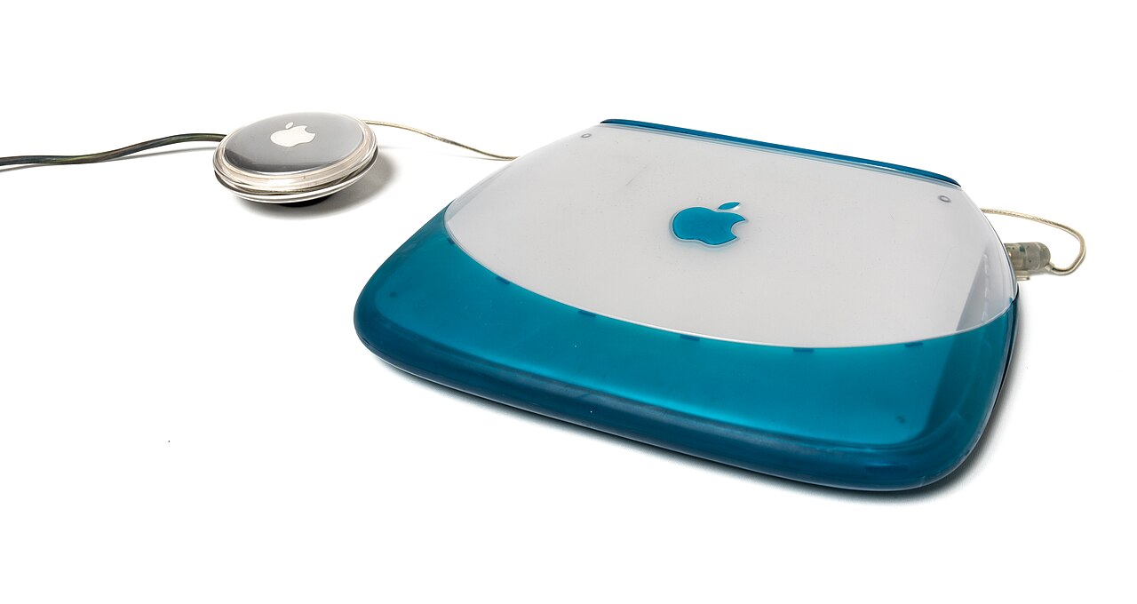 Apple iBook G3 laptop, translucent blue rubberised shell, seen from above with round puck mouse beside it