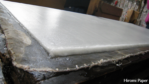 Documentary photograph: a stack of freshly formed wet sheets, squared along one edge on the press bed.