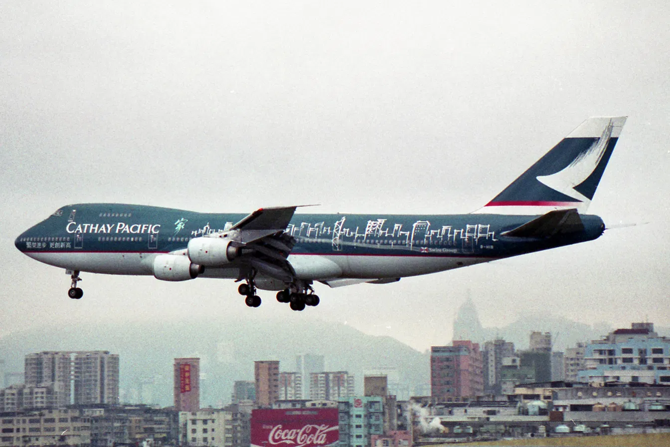 Cathay Pacific Boeing 747 in a heritage livery with the Hong Kong skyline traced in white line-work along the fuselage, landing over the city.
