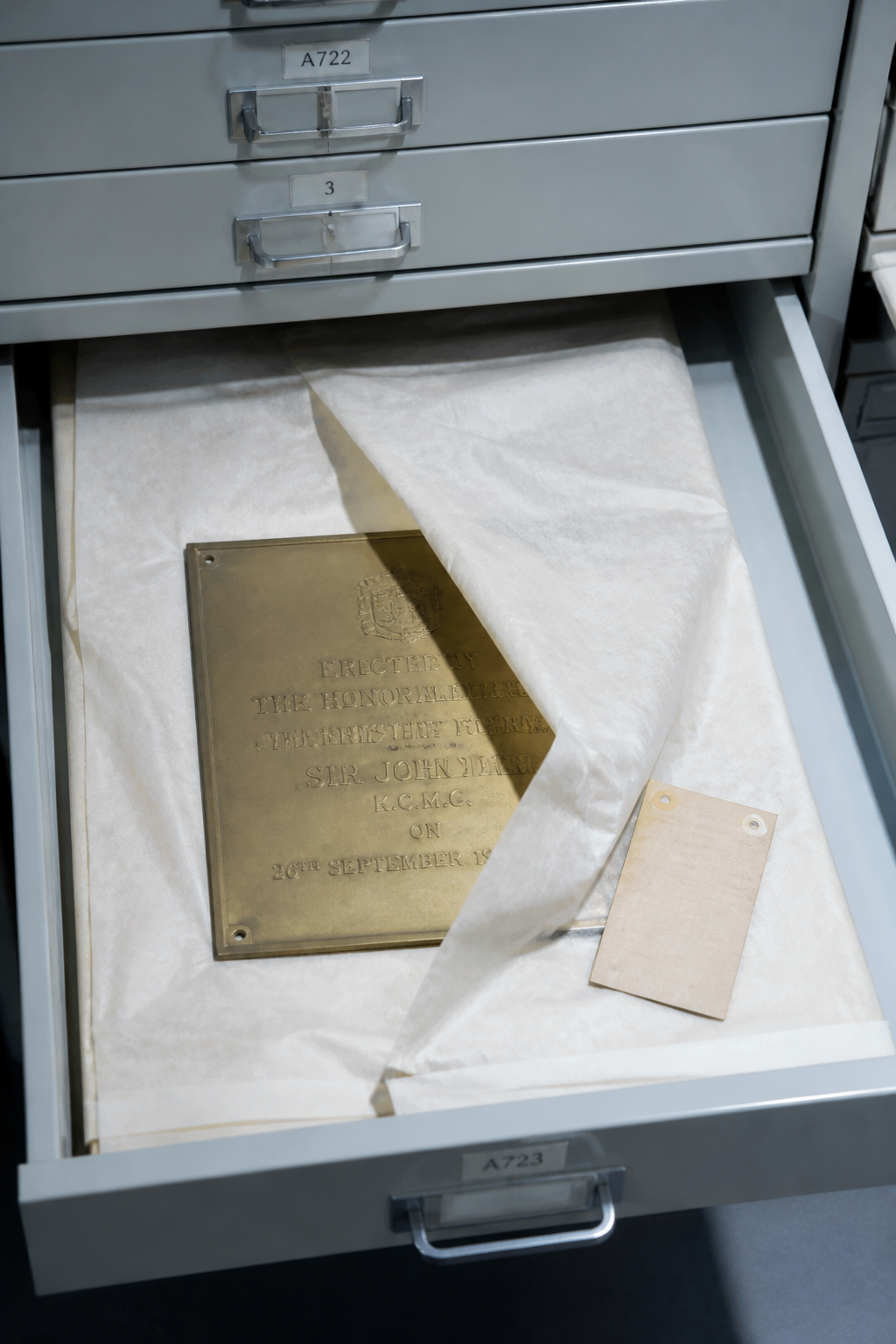 A shallow museum storage drawer: cut foam cradles, a numbered tag, cold even light.